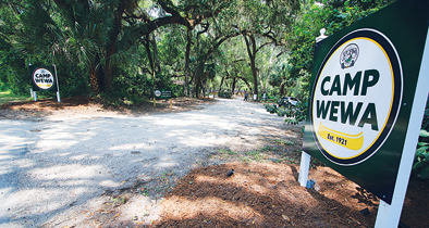 A sign saying "Camp Wewa" stands on the right-hand side of the road going into the campsite.
