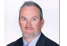 Headshot of a man with a gray beard and hair in a collared shirt, tie and jacket.