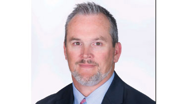 Headshot of a man with a gray beard and hair in a collared shirt, tie and jacket.