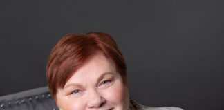Woman sits in chair with one hand on side of her head and looks at the camera.