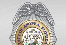 A logo of the Apopka Police Department resembling a bad, with gray and gold colors, and city of Apopka seal in the center.