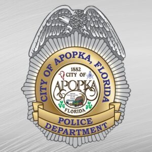 A logo of the Apopka Police Department resembling a bad, with gray and gold colors, and city of Apopka seal in the center.