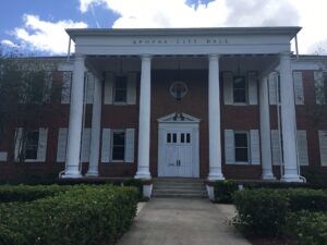 Brick building with multiple windows and columns and works "Apopka City Hall" on the front.