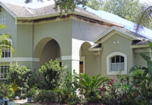 A neutral-colored house with windows and shrubbery in the front. Burns from a fire mark the edges underneath the house's roof.