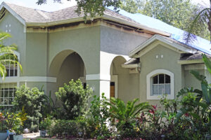A neutral-colored house with windows and shrubbery in the front. Burns from a fire mark the edges underneath the house's roof.