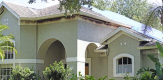 A neutral-colored house with windows and shrubbery in the front. Burns from a fire mark the edges underneath the house's roof.