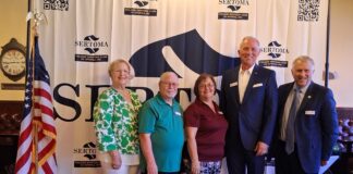 Five people -- two women and three men -- stand in front of the Sertoma Club seal, with the U.S. flag to the left.