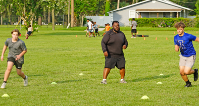 Former president of Apopka Pop Warner, Tony Shuler (c), encourages his players during a shuttle drill.
