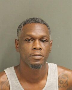 A mugshot of a man in a white sleeveless shirt.