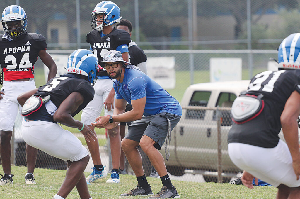 Marcus Neeson squats down into an athletic position and shows his players a drill.