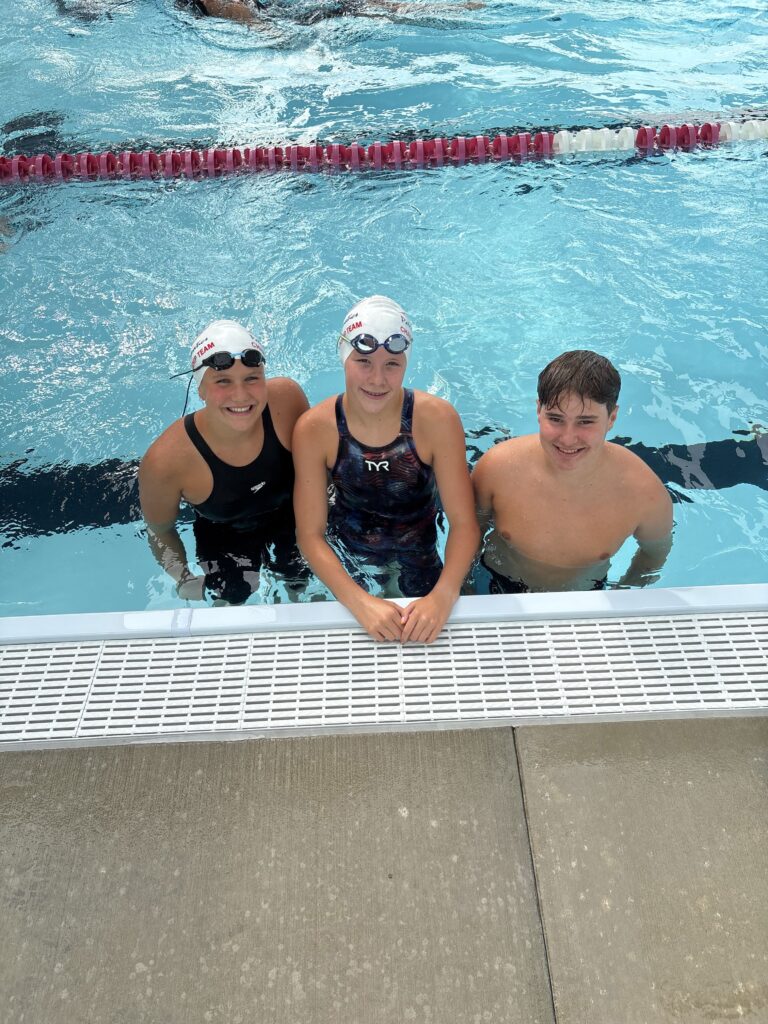 Three swimmers stand together waist-deep in a pool.