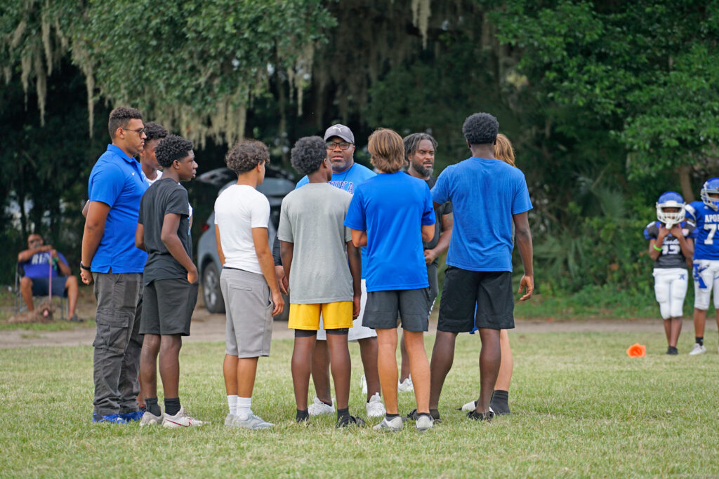 A group of young men talk to an older man as he instructs how to help with drills.