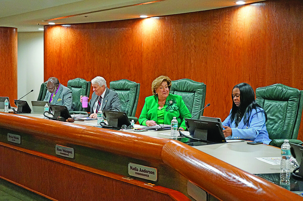 Four people -- two men, two women -- sit on the dais in City Hall.