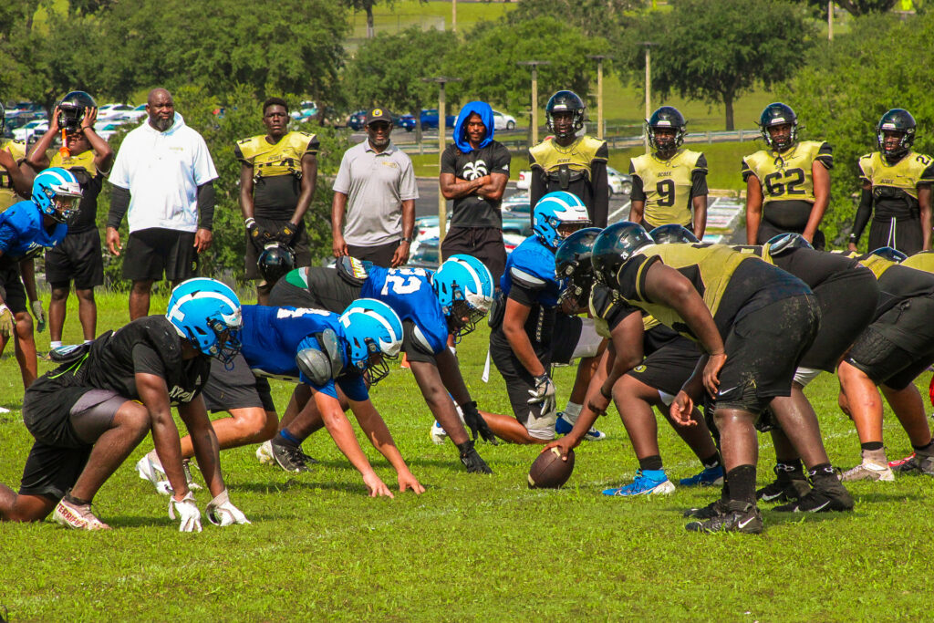 A group of high school football players line up across from each other on the line of scrimmage in full pads.