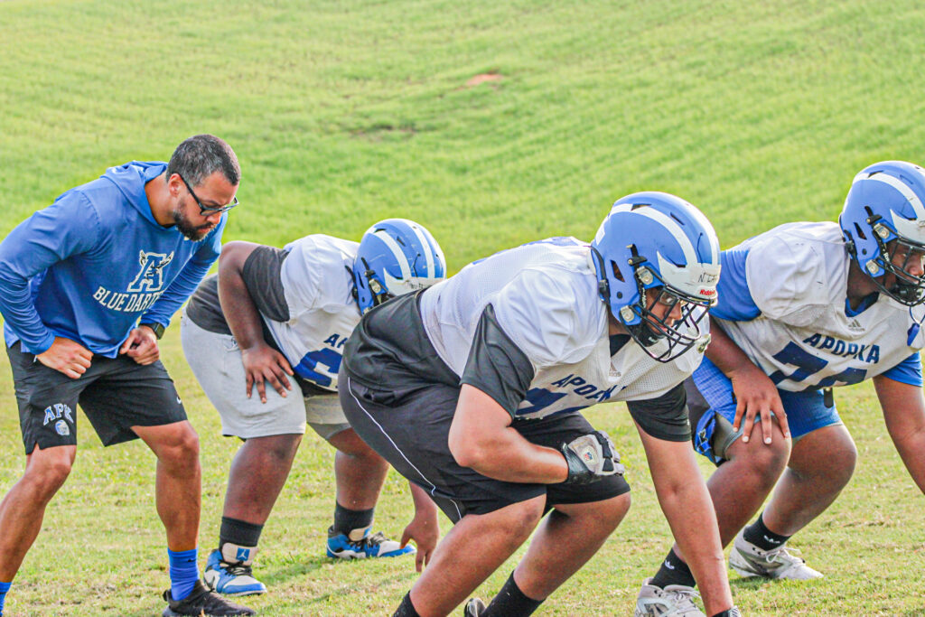 A coach lines up with three of his players as he walks them through a drill.