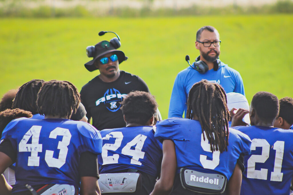 A group of high school football players faces two of their coaches during a timeout.