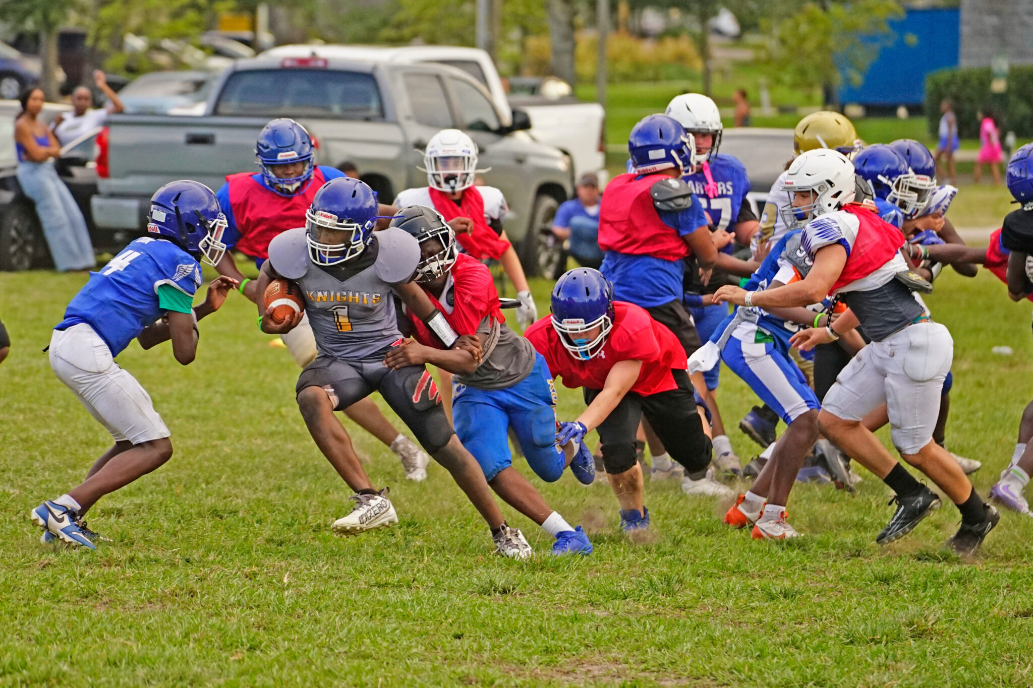 A scrimmage at an Apopka Pop Warner practice shows a running back being dragged down by a group of defenders.