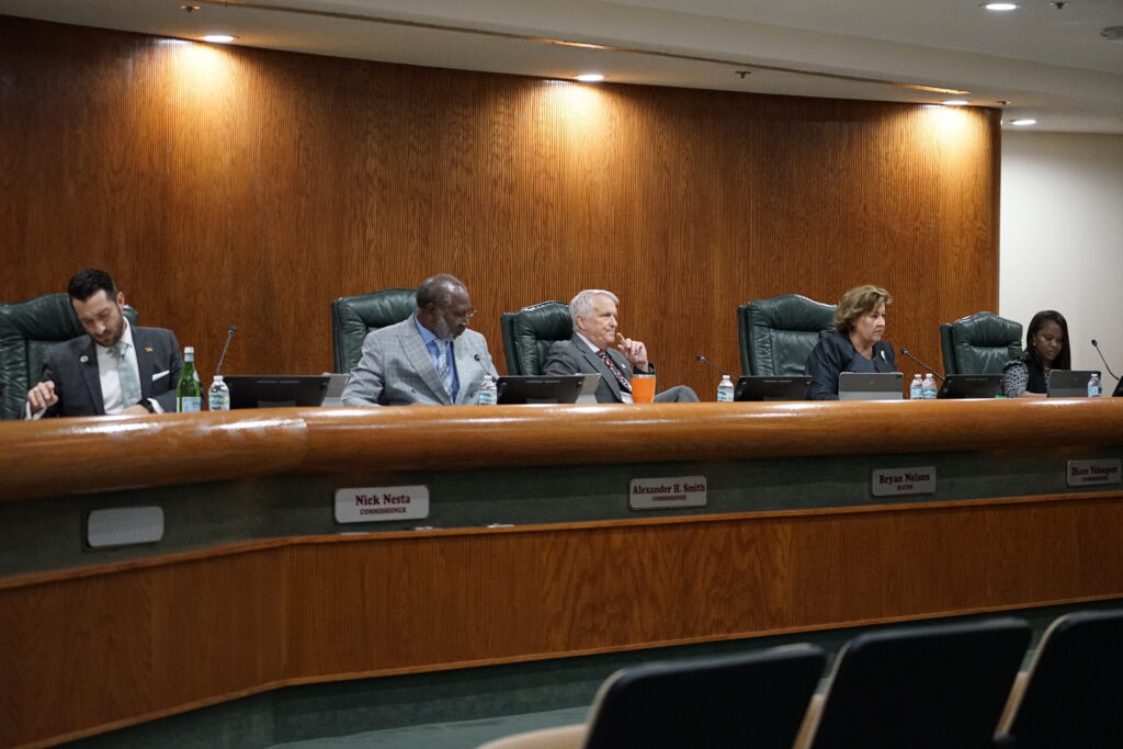 Five people sit on a dais with a desk in front of them.