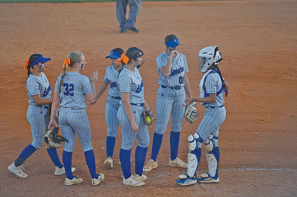 A group of young girls in softball uniforms surrounds the pitcher during an Apopka High School game.