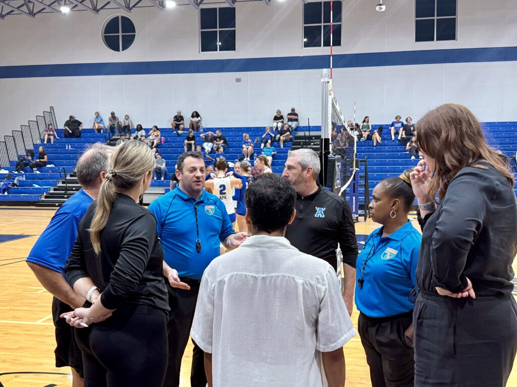 Coaches, referees, and Athletic Director huddled at mid court.