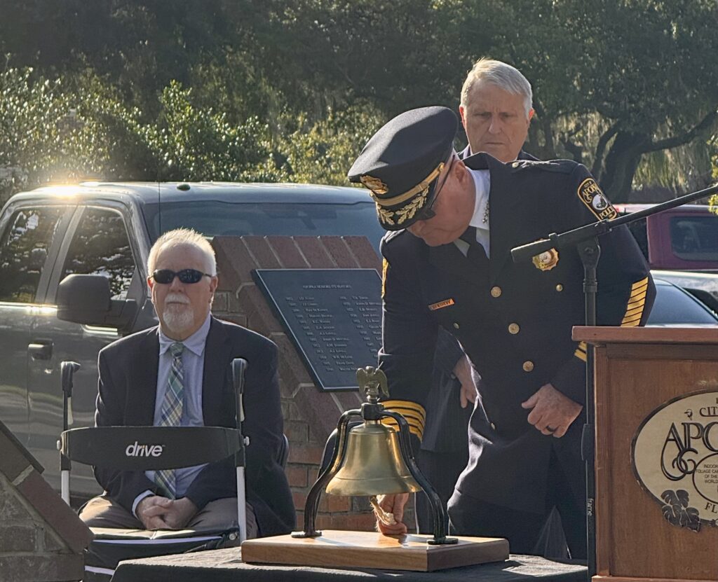 Apopka Police Chief Michael McKinley rings a bell to honor the fallen as Pastor John Fisher and Mayor Bryan Nelson look on.