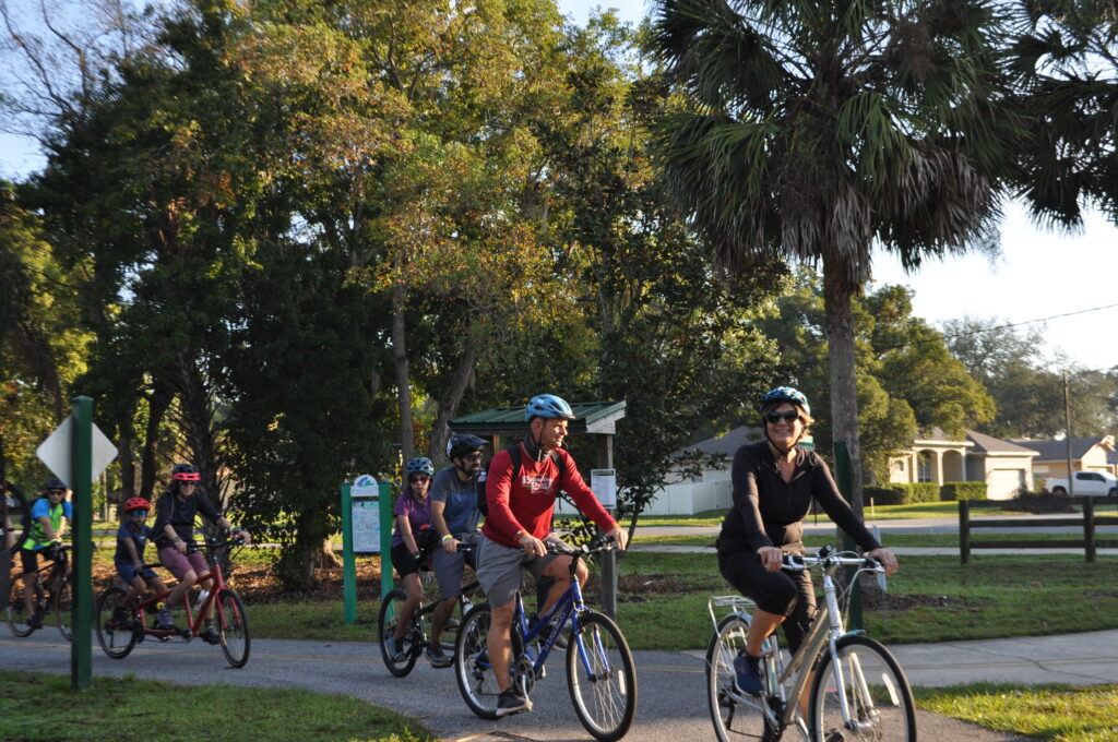 Several people ride their bikes in the daytime. Trees are in the background.