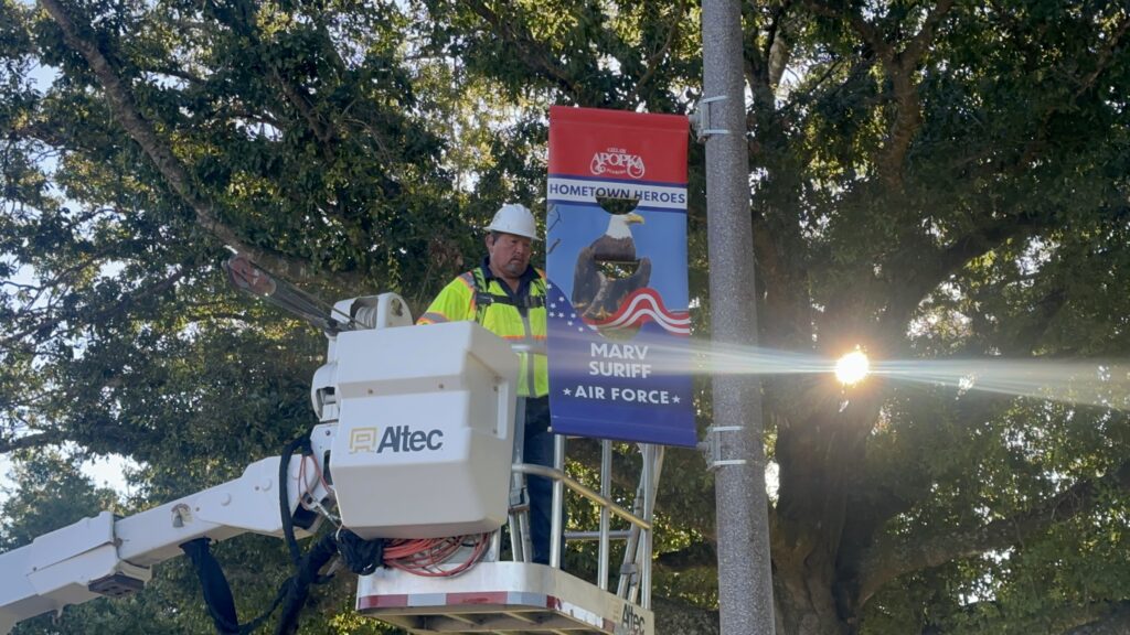 A city worker mounts Marv Suriff’s banner on a pole in front of Apopka City Hall.