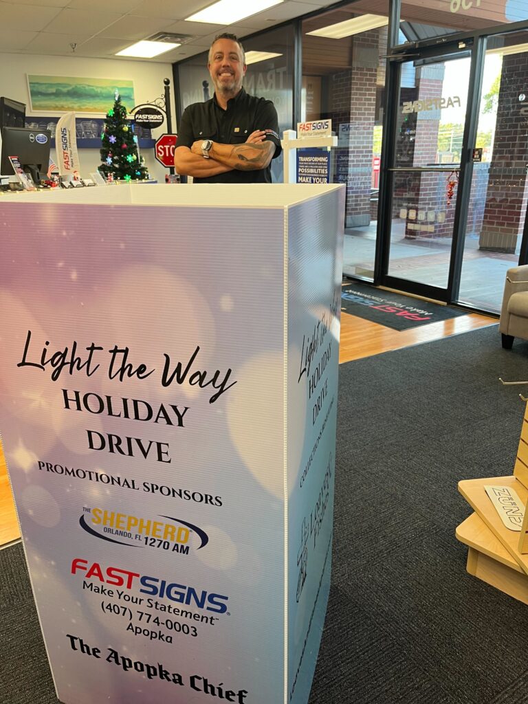 Charles Chambers of FASTSIGNS Apopka smiles behind a donation box.