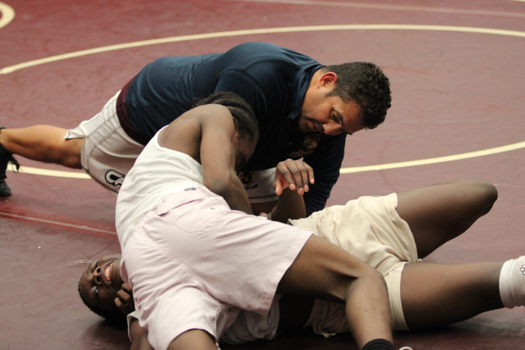 Coach Lenin Vazquez guiding Jeremiah Demosthene through a hold