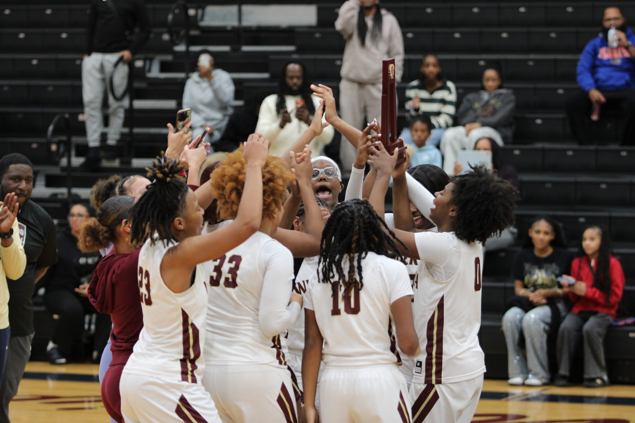 Lady Mustangs huddle and raise their trophy at center court