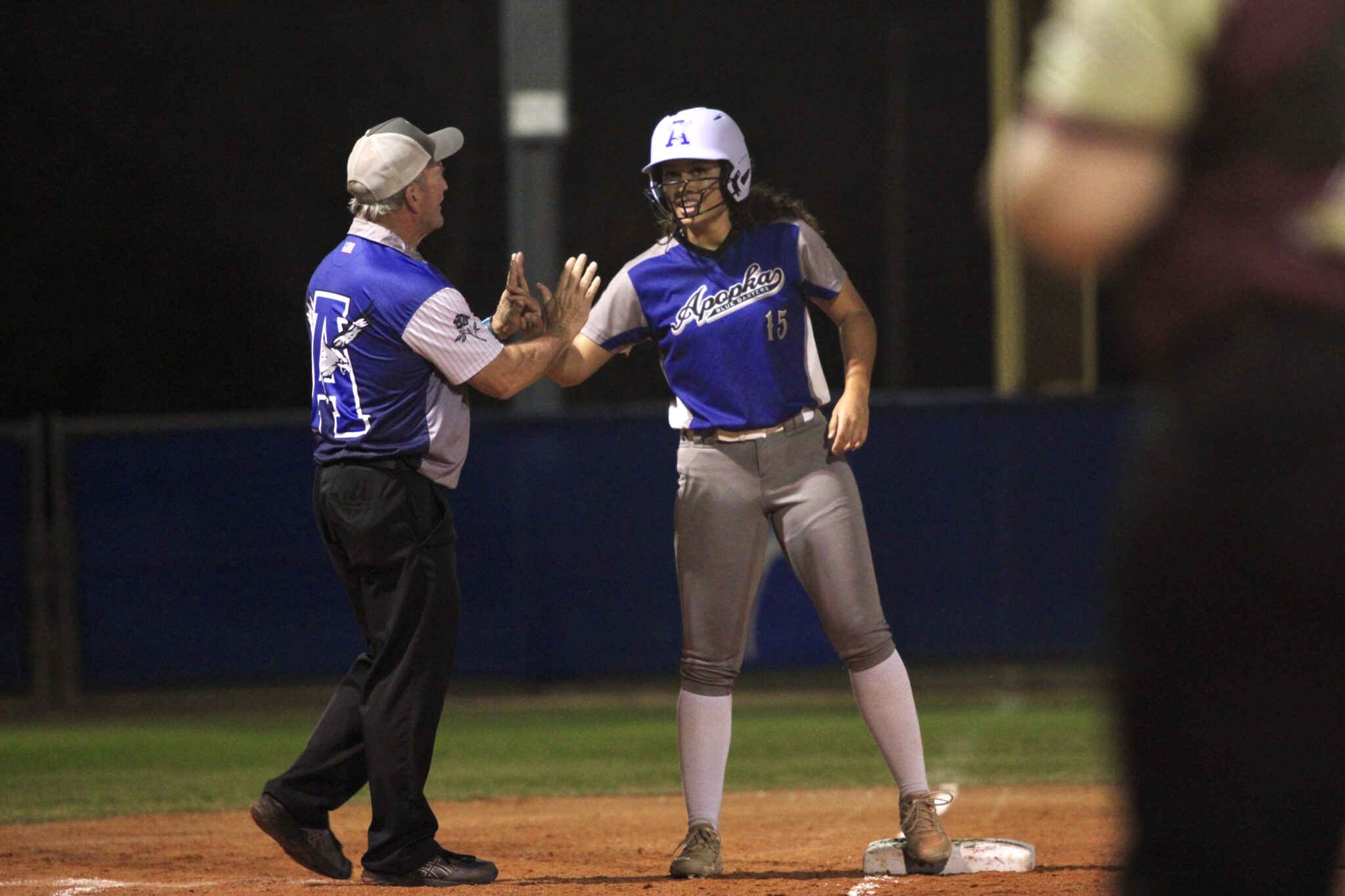 Coach Mike MacWithey greets Victoria Shaw at third base with high fives after her steal