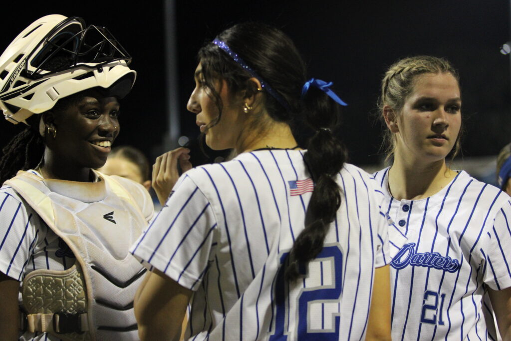 Taylor Smith, Mia Aeschilman, and Ava Millspaugh huddle after an inning