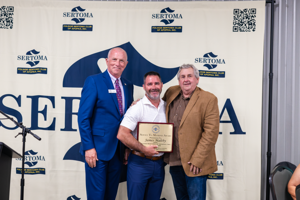 Foliage Sertoma Club of Apopka president Eric Mock (left) and sports commentator Roger Franklin Williams (right) pose with James Maltby, the 2026 Service to Mankind Award winner, at the April 28 Sertoma dinner.