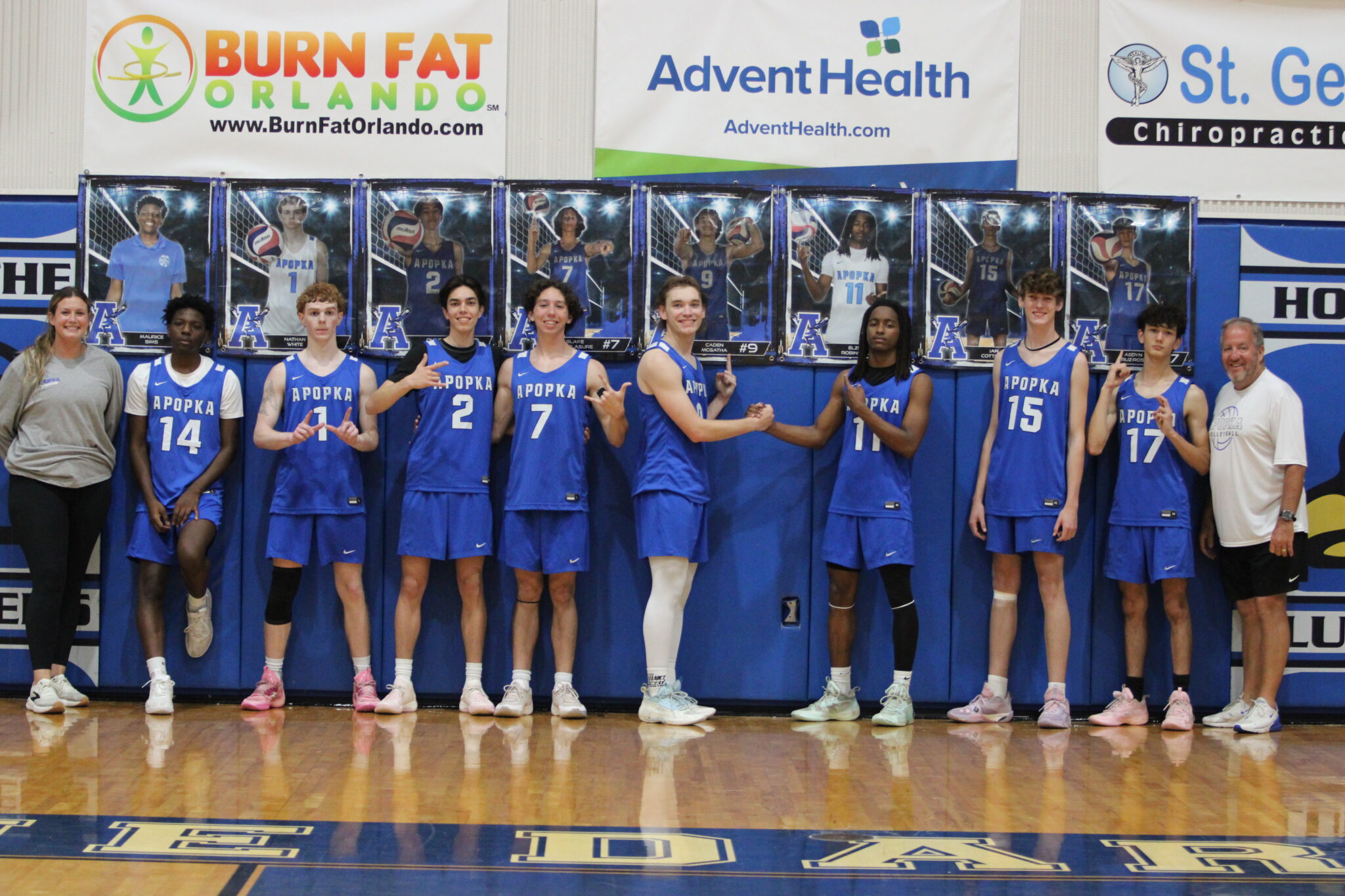 Blue Darters pose with their coaches under their senior night photos after their sweep against Olympia