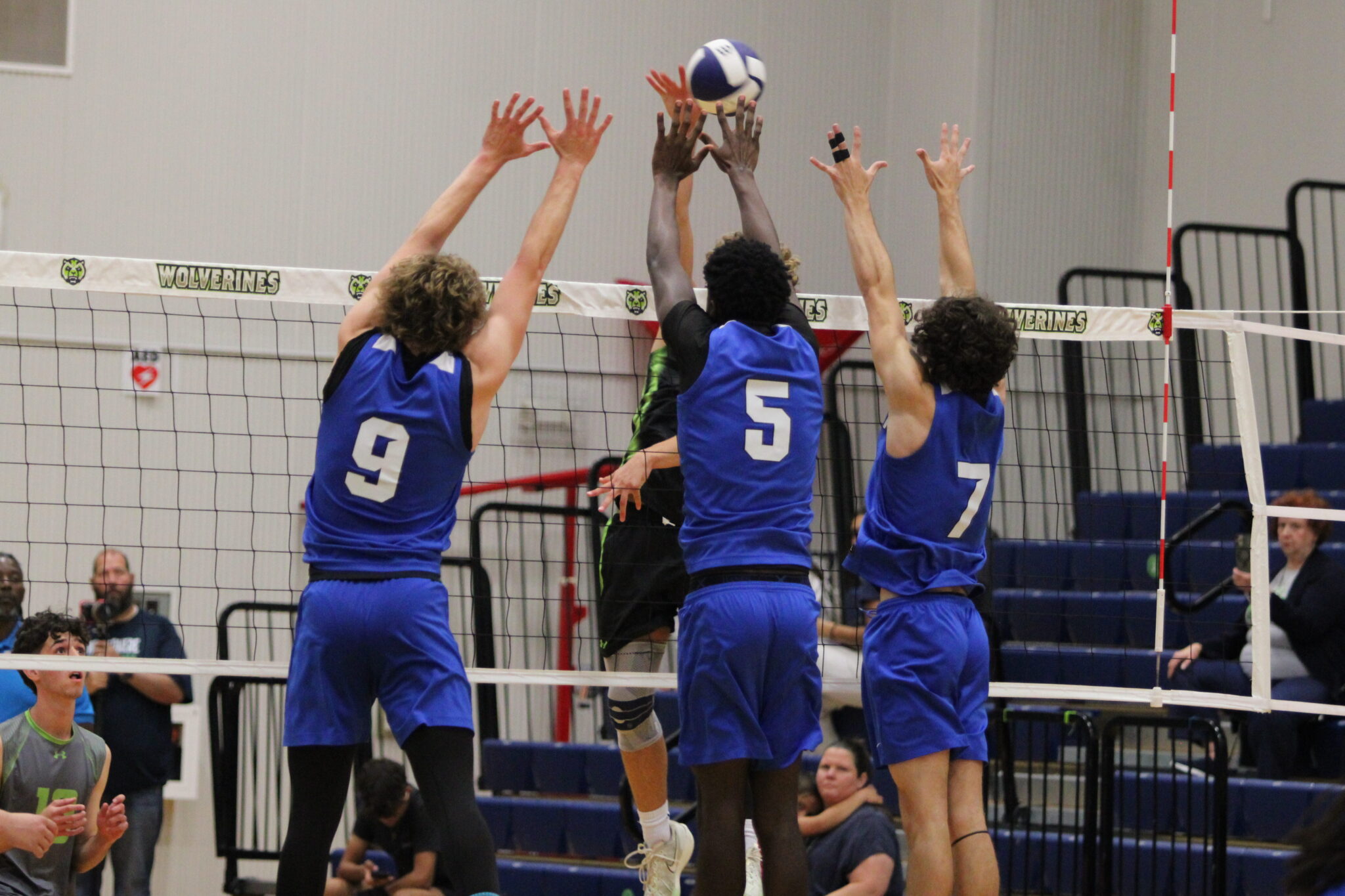 Caden McGatha, Giovanni Lubin, and Blake Colclasure leap up and create a wall of hands at the net