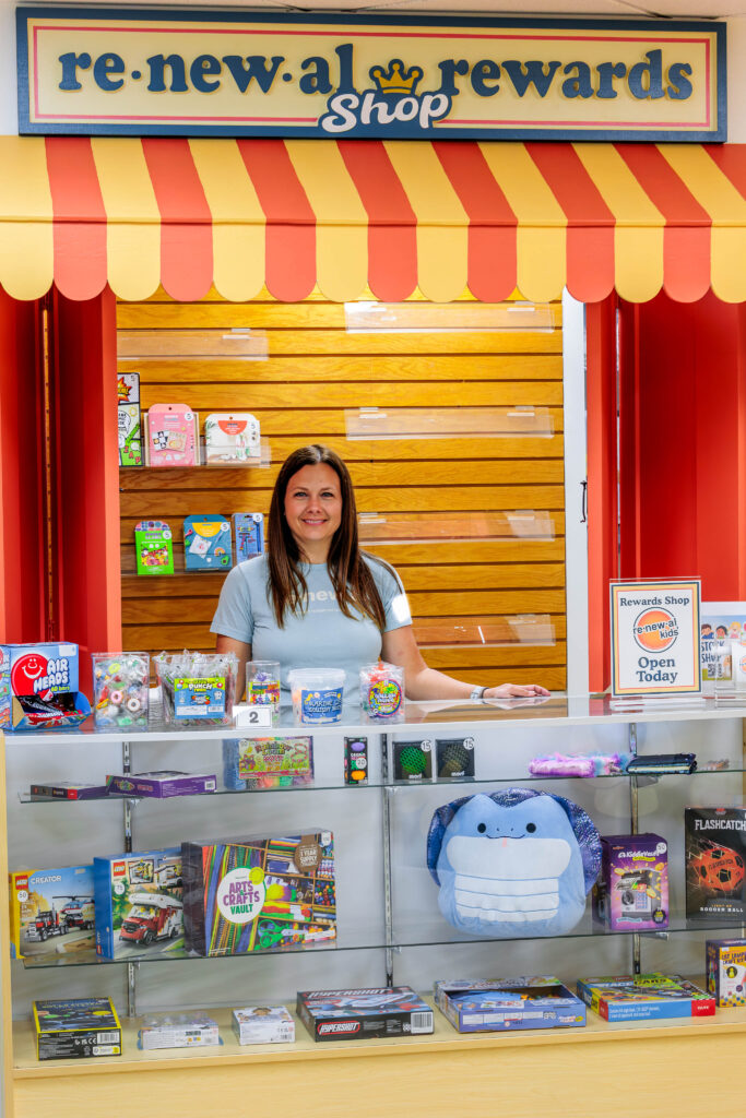Renewal Kids leader Traci Kieffer stands behind the counter at the Renewal Rewards Shop, where children spend the Disciple Dollars they earn by learning in the classroom.