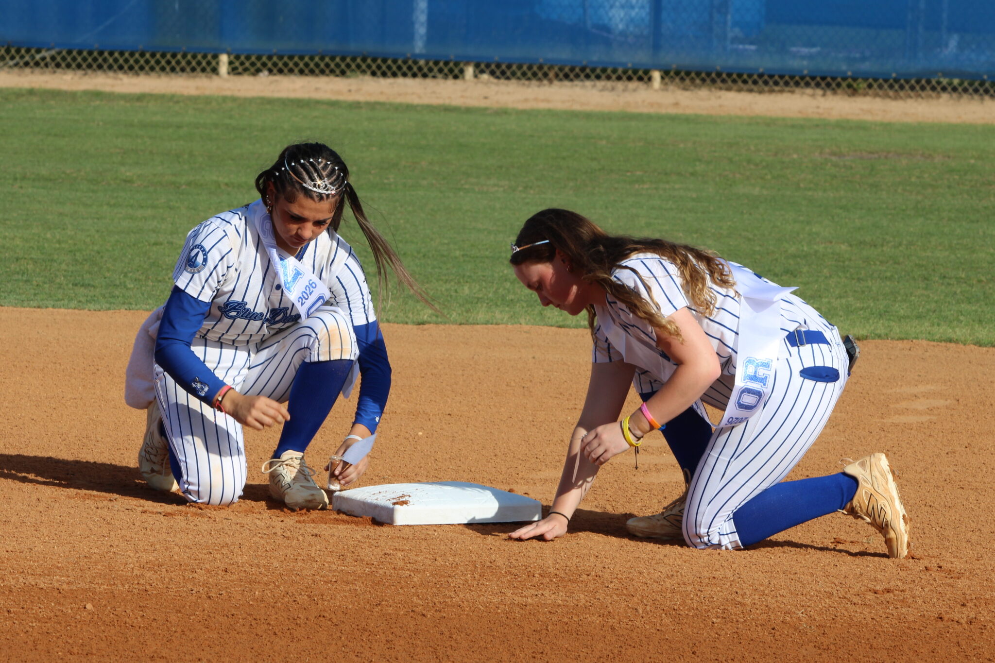 Shylah Pino and Riley Ford collect dirt at second base in memorial of their time on the field