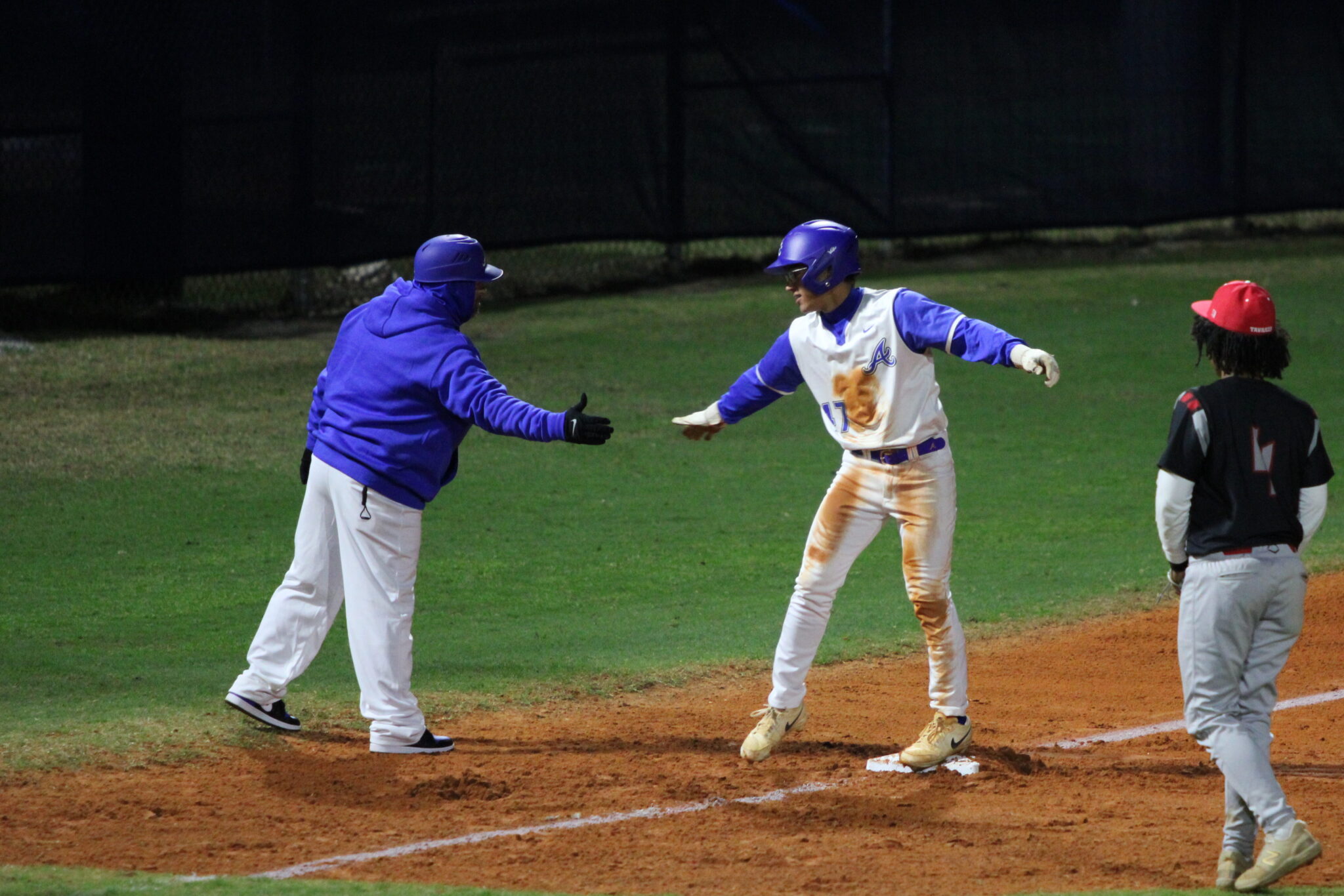 Coach Scott Garland at third base gives Ty Livingston five after his triple