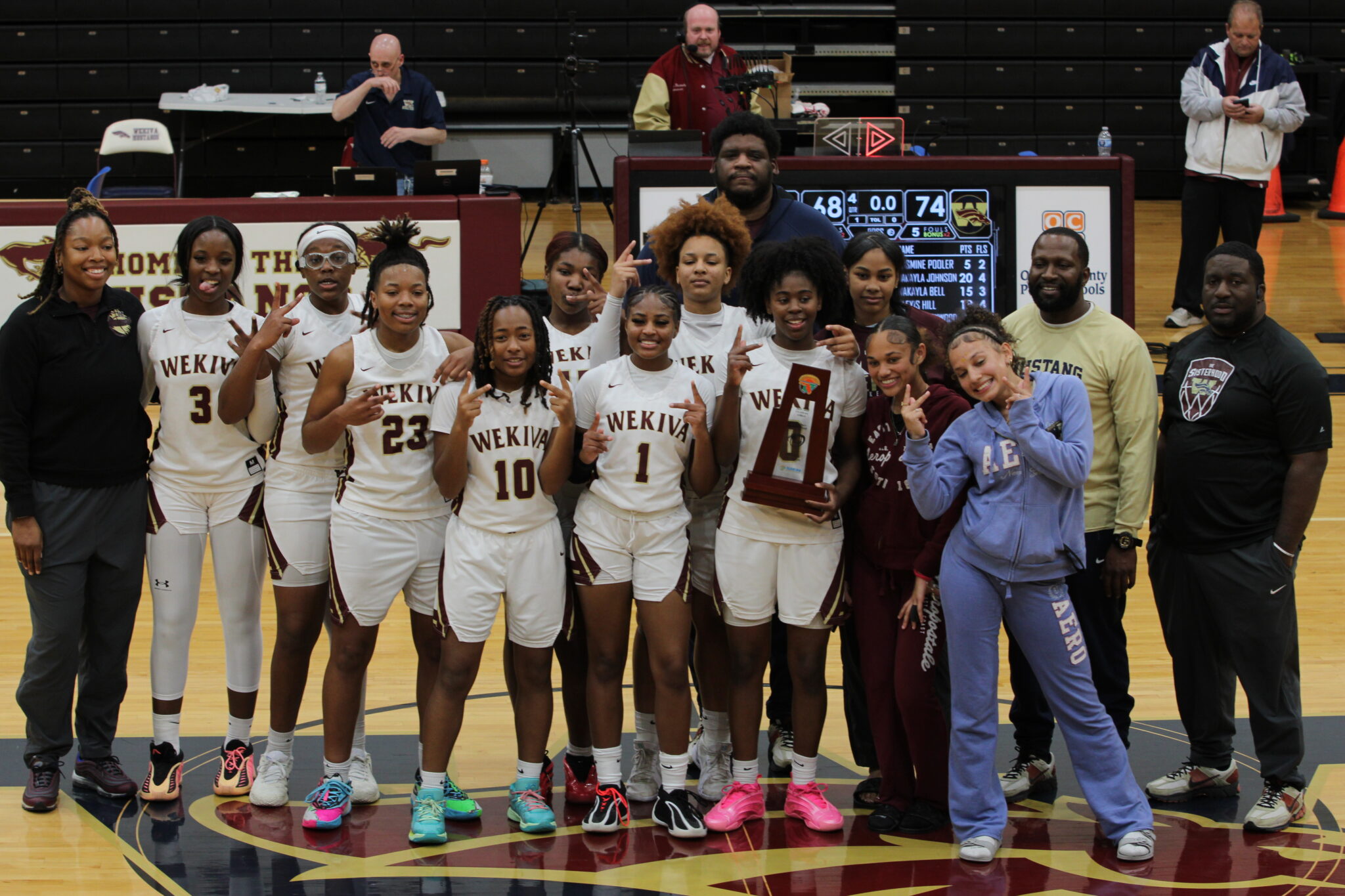 Lady Mustangs basketball pose on home court with the district championship trophy.
