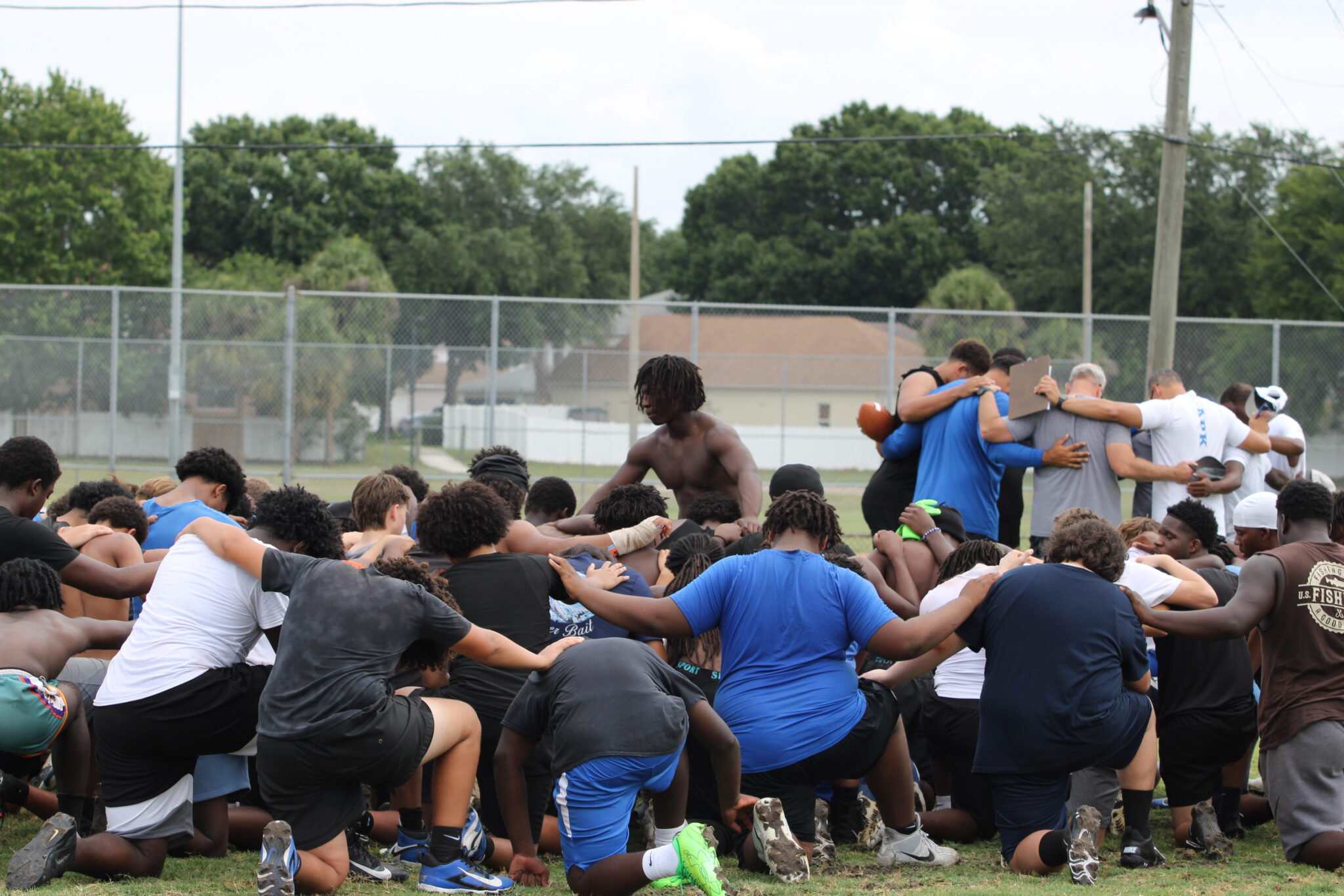 Players and coaches huddle in separate group prayers at the end of practice.
