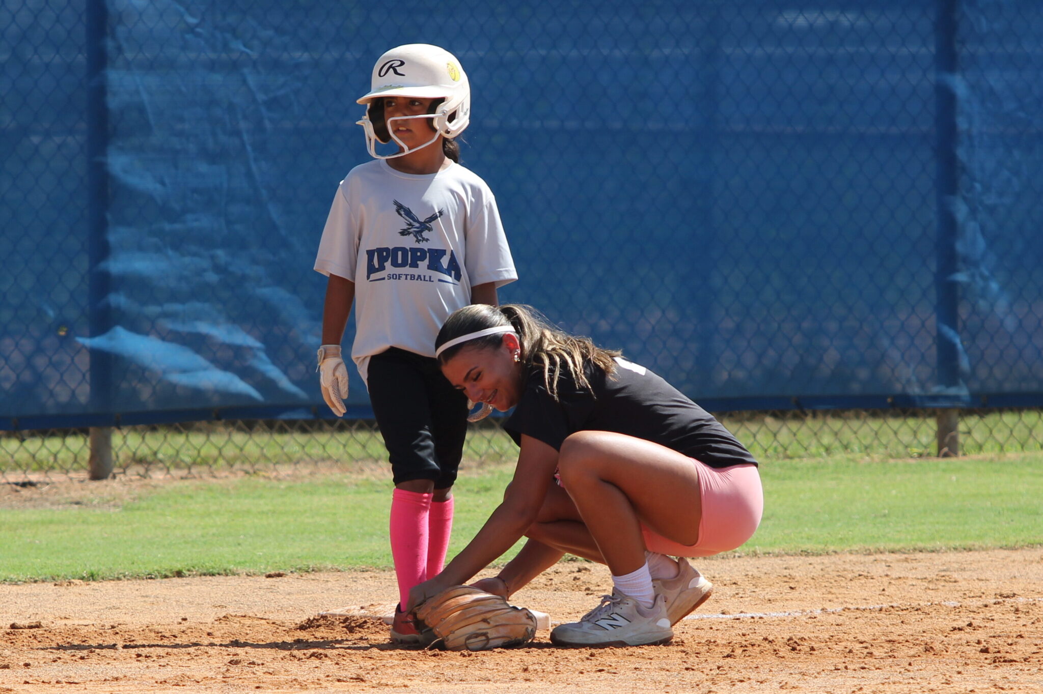 Blue Darter alum and West Alabama freshman, Shylah Pino, helps a young baserunner tie her shoe at third base on Wednesday at the Apopka softball camp.