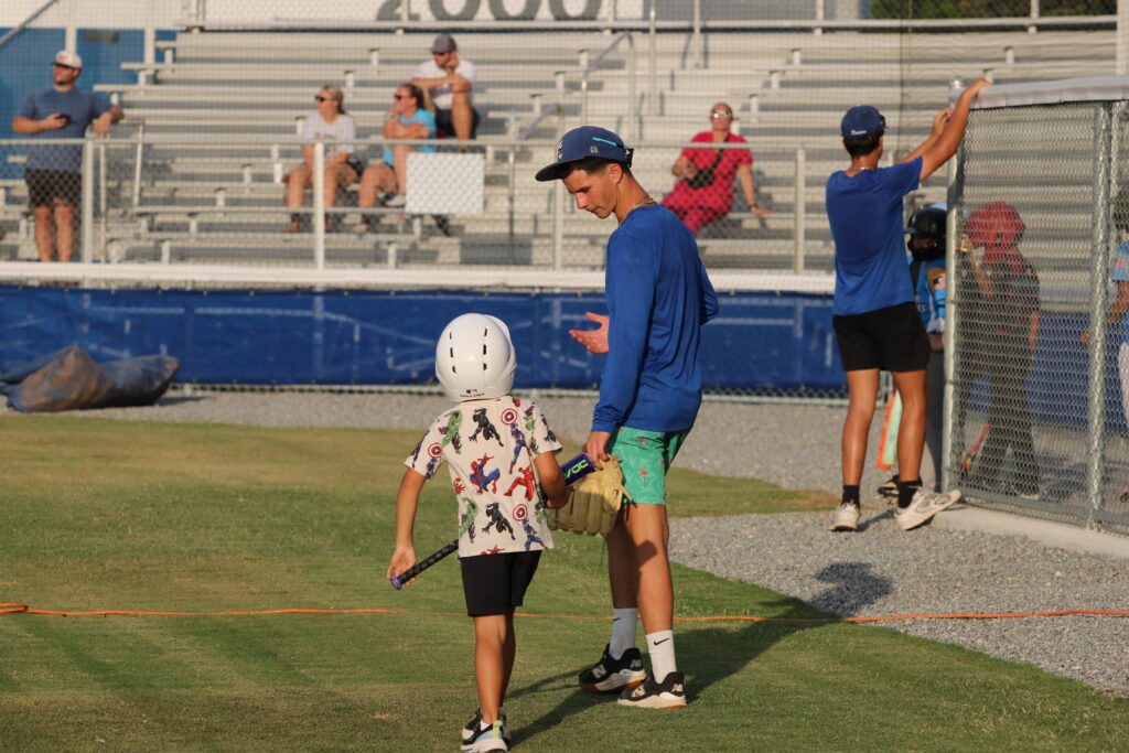 Blue Darter junior Zackary Lovejoy walks with and instructs a young camper on his walk to the plate for his at-bat.