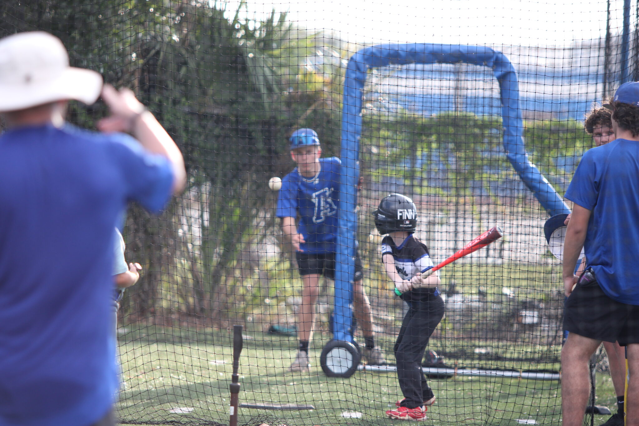 Blue Darter player throws a soft toss to a camper in the 5-6-7 group in the batting cages.