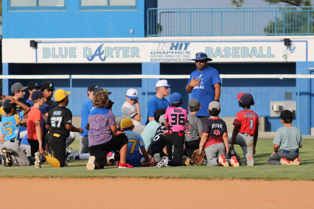 Coach Scott Garland huddles the campers on the infield grass to instruct them.