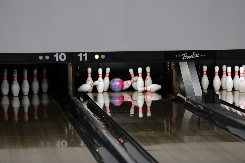 A bowling ball rolled by the hands of a Blue Darter crashes through a set of pins.