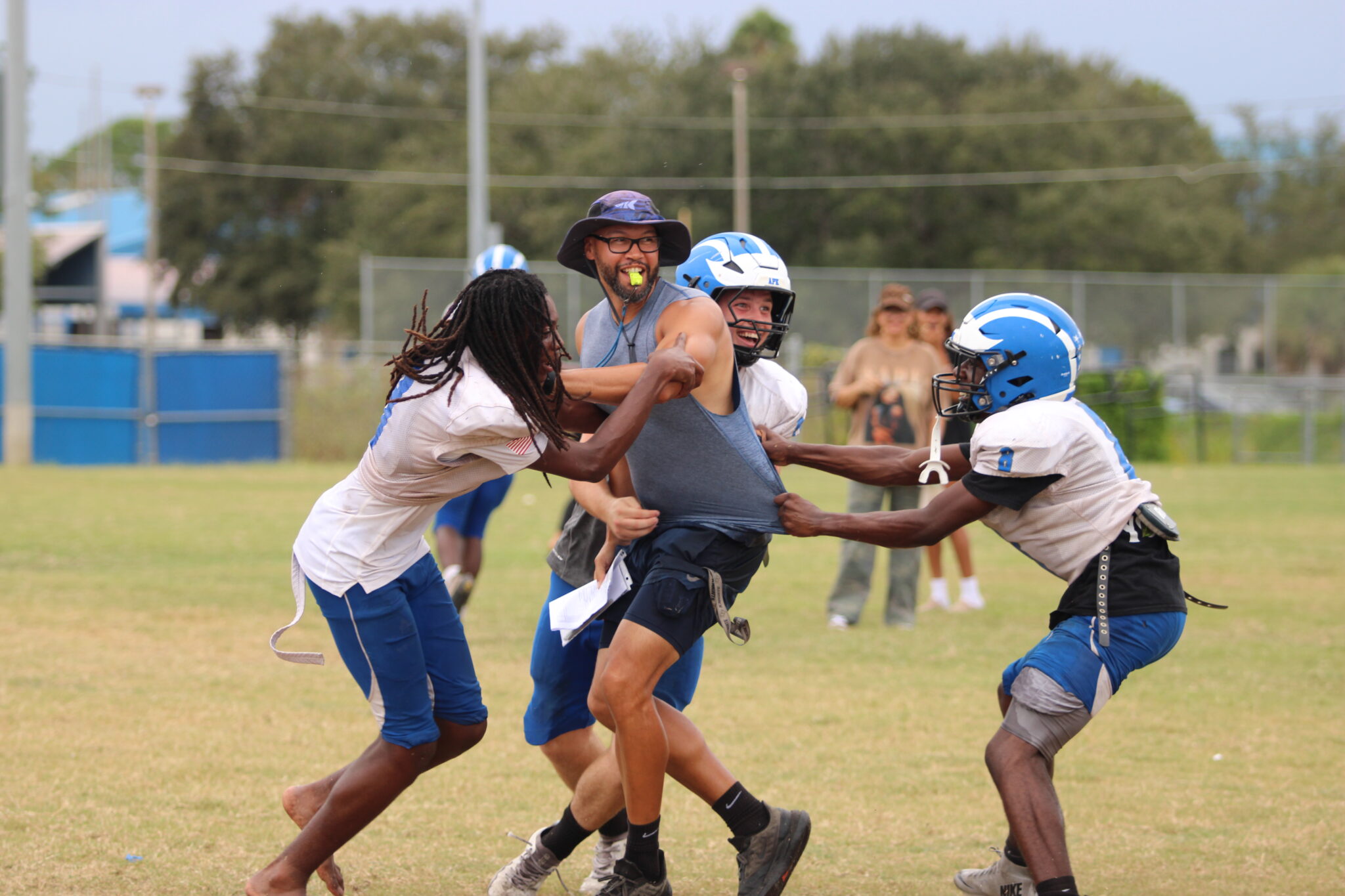 Blue Darters grab Coach Neeson in attempt to dump a water balloon cooler on him.