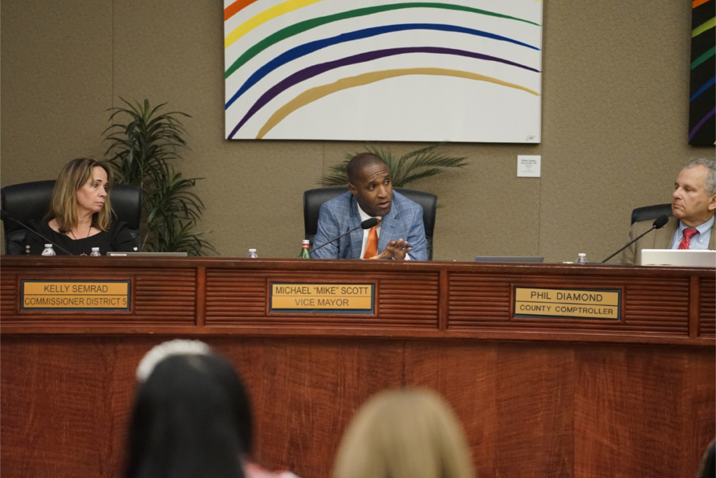Orange County Commissioner Michael Scott, center, speaks during a 2025 commission meeting, flanked by Commissioner Kelly Semrad and Comptroller Phil Diamond.