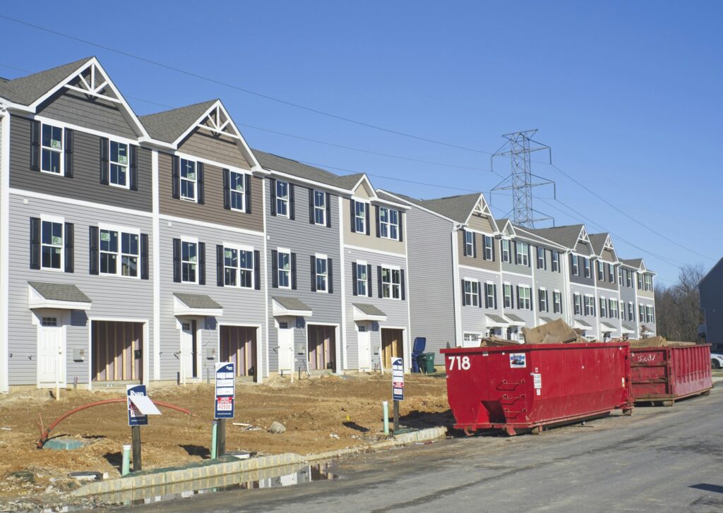 Row of townhouses under construction with red dumpsters at a suburban development site.